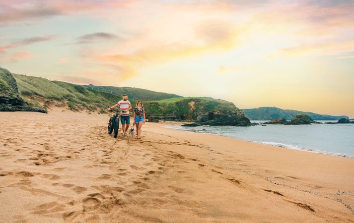 Man and woman strolling along the coast with bicycle and small dog