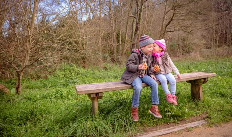 Cute little boy and girl sitting on park bench talking with snack