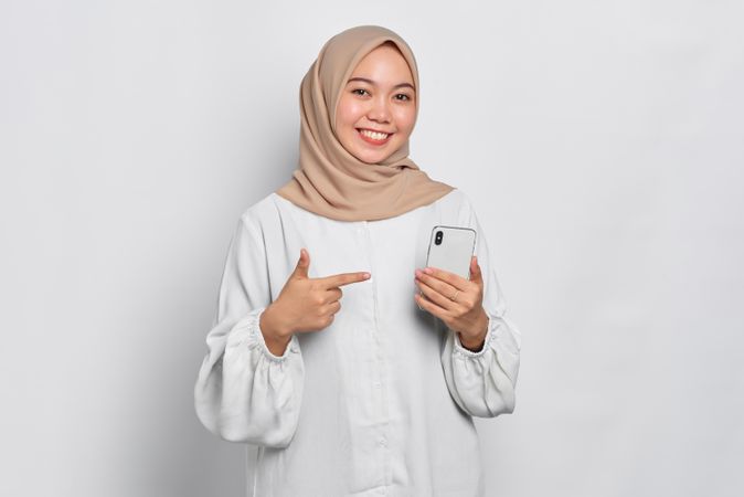 Asian female in headscarf smiling and pointing at cell phone