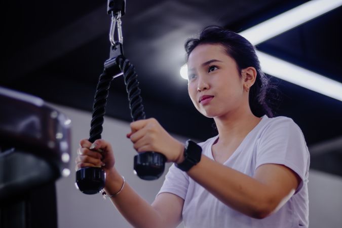 Asian woman strengthening triceps with a cable rope in fitness club