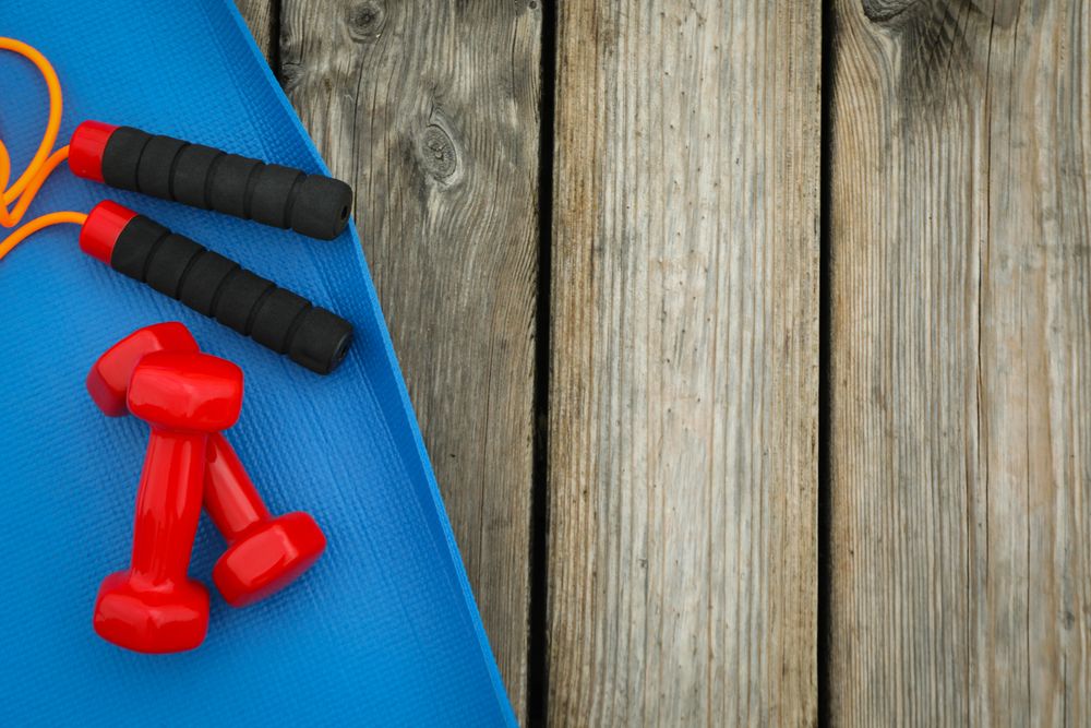 Karemat, jump rope and dumbbells on wooden background, space for text