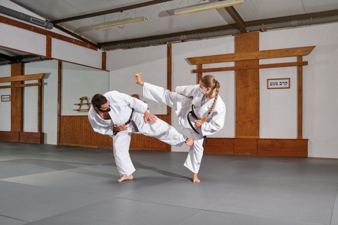 Two people with mask and kimono practicing krav maga kicks in a