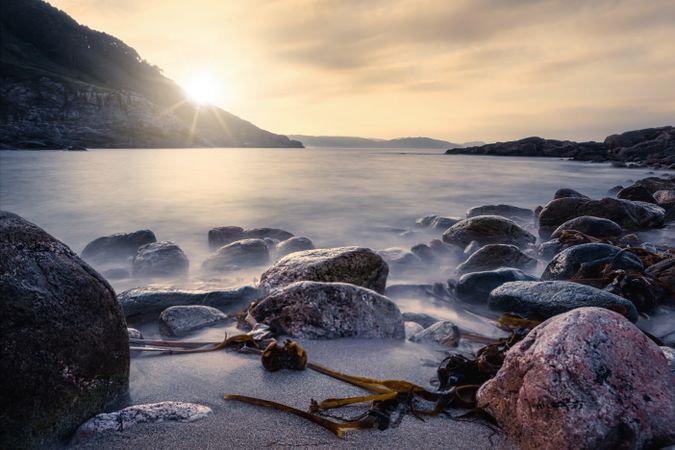 Landscape of rocked seashore with rising sun on cloudy sky