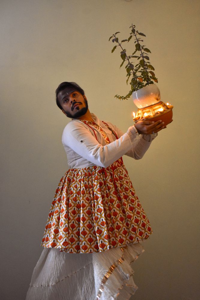 Indian man in kathak dress holding plant with diyas and dancing