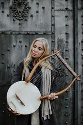 Pensive charming woman holding lyre at metal gates
