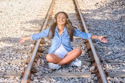 Smiling woman listening to music sitting on railroad