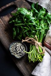 Arugula and sesame seeds on cutting board with kitchen towel