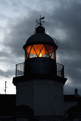 Shining lighthouse against cloudy sky