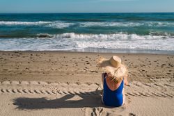 Woman in blue swimsuit and hat on sandy beach