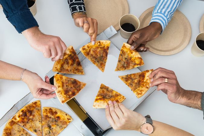 Crop diverse friends eating pizza during meeting