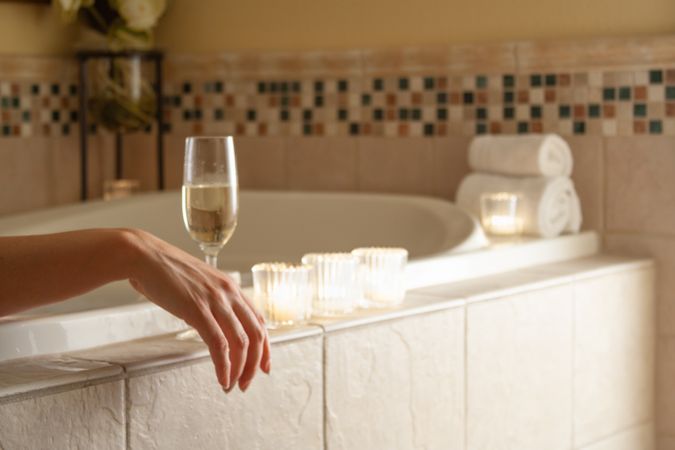 Woman Relaxing in the Bathroom Spa Tub with a Glass of Sparkling Champagne and Candles.