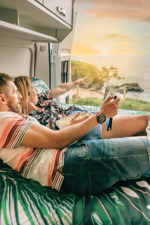 Male and female on bed in motorhome enjoying the view with popcorn and digital tablet, vertical