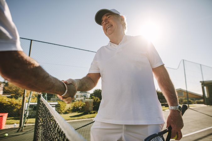 Happy man shaking hand of male over a tennis net