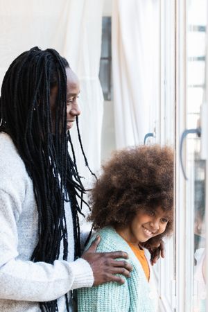 Black father with daughter standing near window