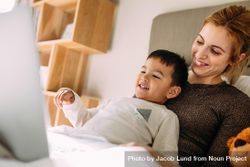 Smiling young woman with a little boy on the bed watching movies on laptop bEpXG4