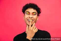 Happy young man wearing rainbow colored eye shadow and smile face nail paint 0yPrWb