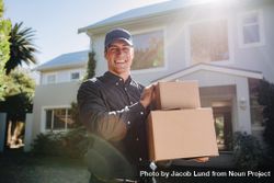 Delivery man standing in front of a house holding two cardboard boxes 4M2vqb