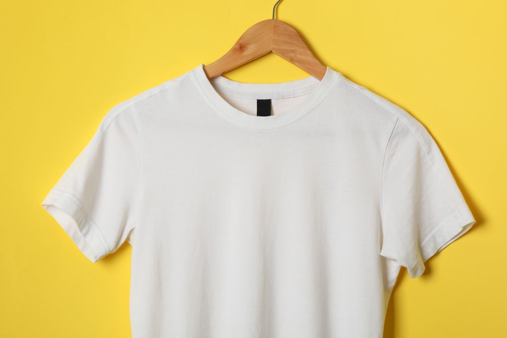 Hanger with blank plain t-shirt on yellow background, space for text