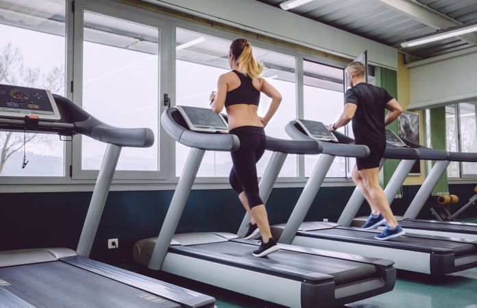 Back of fit man and woman jogging on treadmill