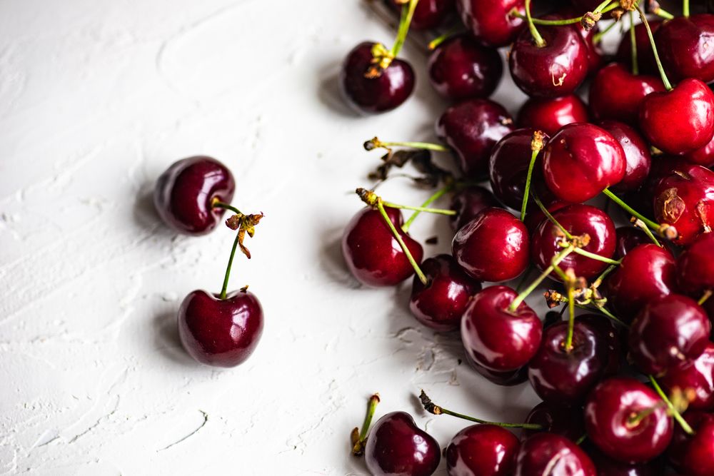 Top view of scattered sweet cherries on grey kitchen counter with space for text