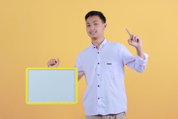 Portrait a young man in yellow backdrop holding a blank note board