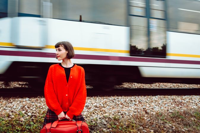 Woman watching moving train behind back on railroad