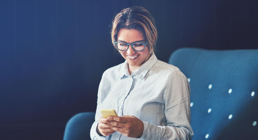Female businesswoman smiling at phone while sitting on sofa