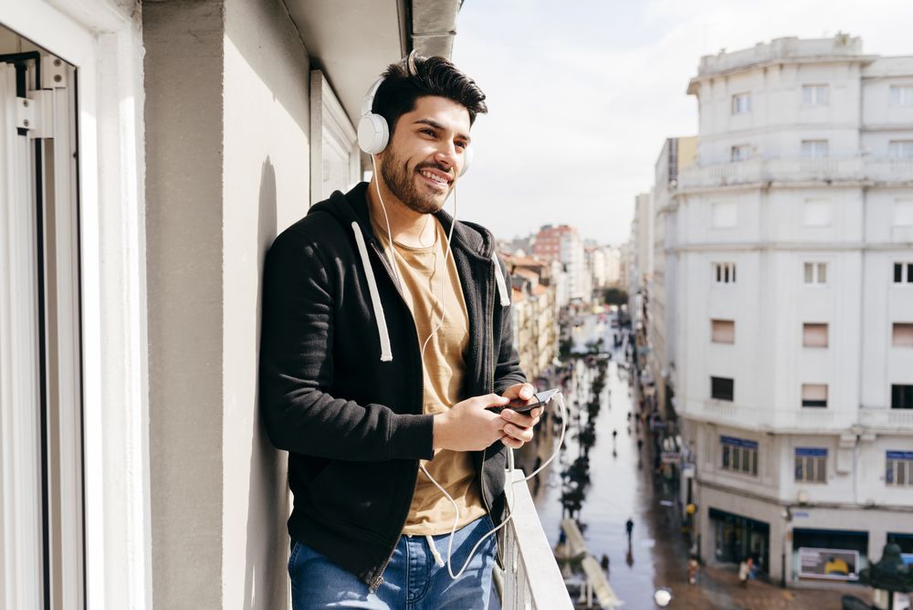 Young happy man holding smartphone on balcony