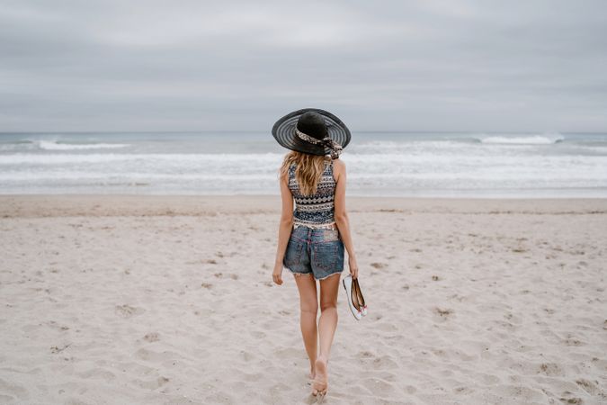 Young female walking barefoot on sandy beach