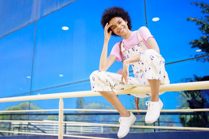 Smiling woman sitting on handrails in front of reflective building