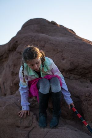 Young girl with braids climbing down a boulder outside
