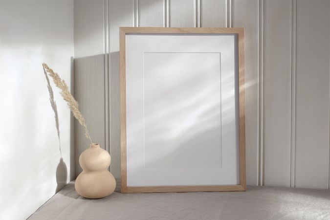 Blank vertical picture frame mock up in sunlight. Modern vase with dry grass festuca.