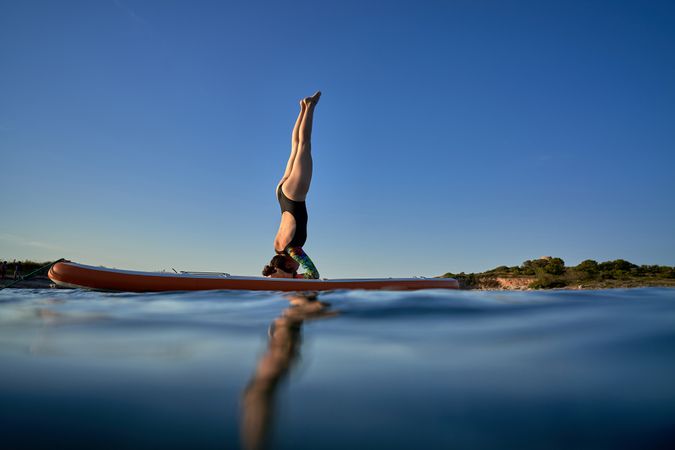 Unrecognizable woman practicing Supported Headstand on SUP board