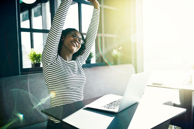 Woman sitting with laptop in cafe and stretching