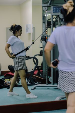 A woman uses a cable machine in a gym, doing an exercise routine