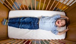 Happy boy lying in a cot with arms and legs stretched
