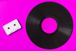 Audio cassette tape and vinyl record on pink background