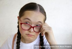 Portrait of young girl looking at camera while holding her eyeglasses away from eyes 0PEwN5