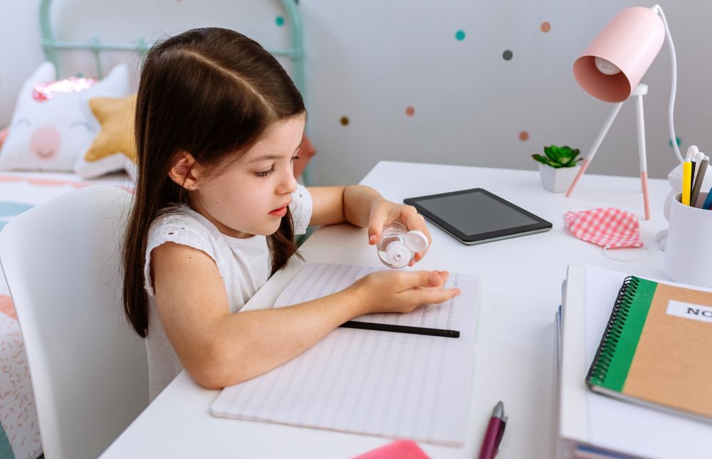 Girl applying hand sanitizer while doing homework