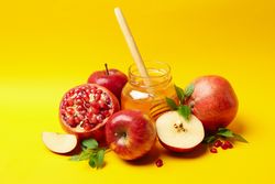 Fresh apples, pomegranate and honey grouped in centered yellow background