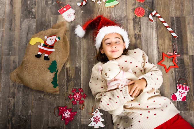 Girl in Santa hat lying on wooden floor surrounded by gifts