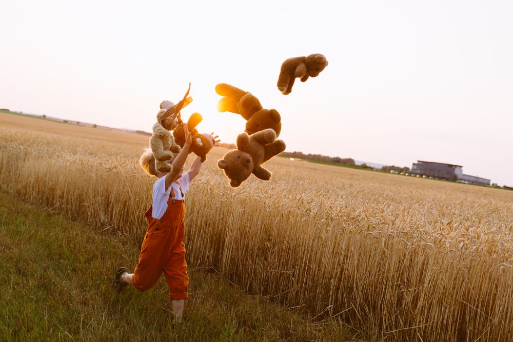 Little boy throwing teddy bears and running on field in countryside