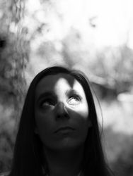 A young woman looks up, with a serious and thoughtful countenance while a ray of light illuminates part of her face