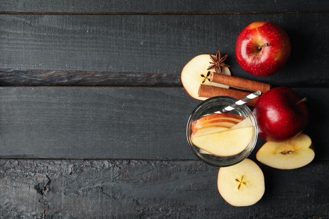 Top view of glass of water with straw, apple slices and cinnamon slices on wooden table