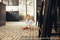 Cute baby sitting on the kitchen floor with hand in mouth 473nP4