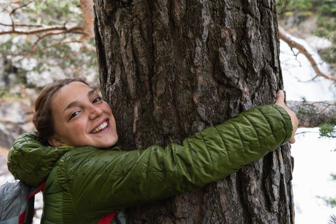 Smiling traveling woman hugging tree in woods
