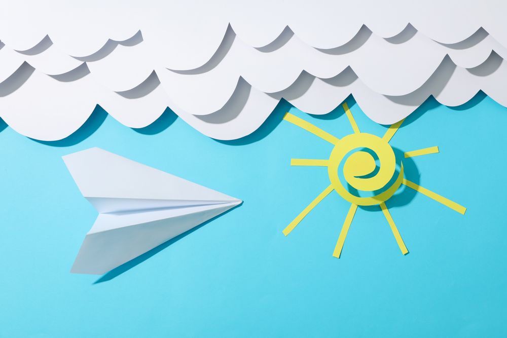 Paper clouds, sun and plane on blue background. Travel