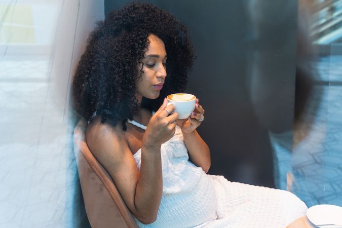Black pregnant woman blowing on cup of hot latte