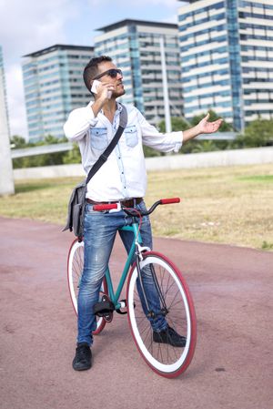 Male with colorful bicycle having animated conversation on phone on city bike path, vertical