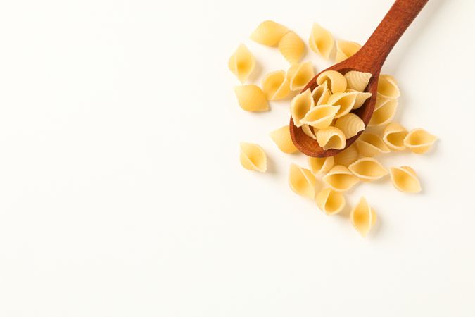 Wooden spoon with pasta on blank background, space for text. Dry uncooked whole pasta